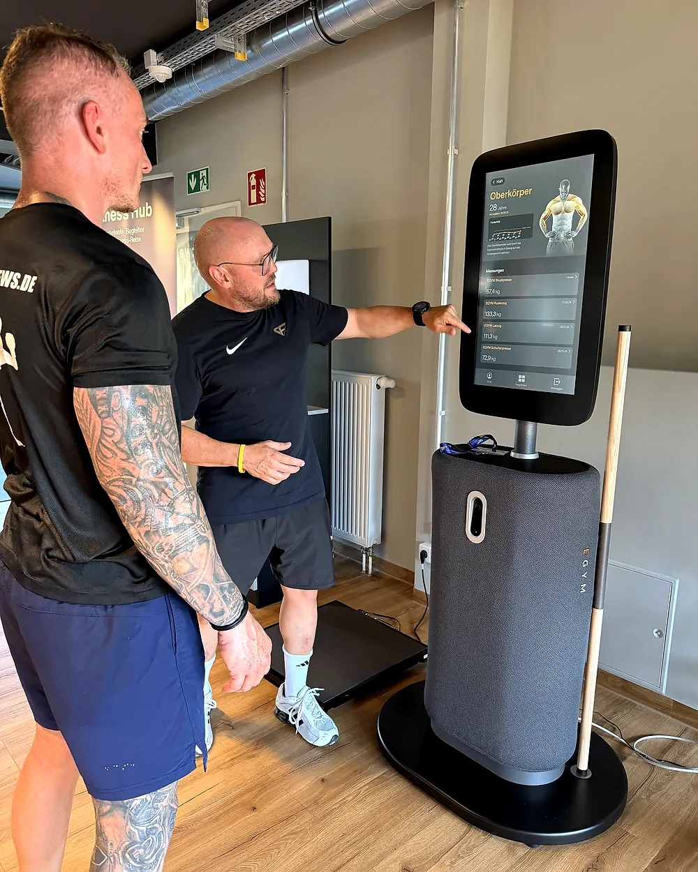 Trainer Mirko erklärt einem Mitglied die EGYM-Oberkörper-Auswertung am Fitness Hub – Lila Fitness
