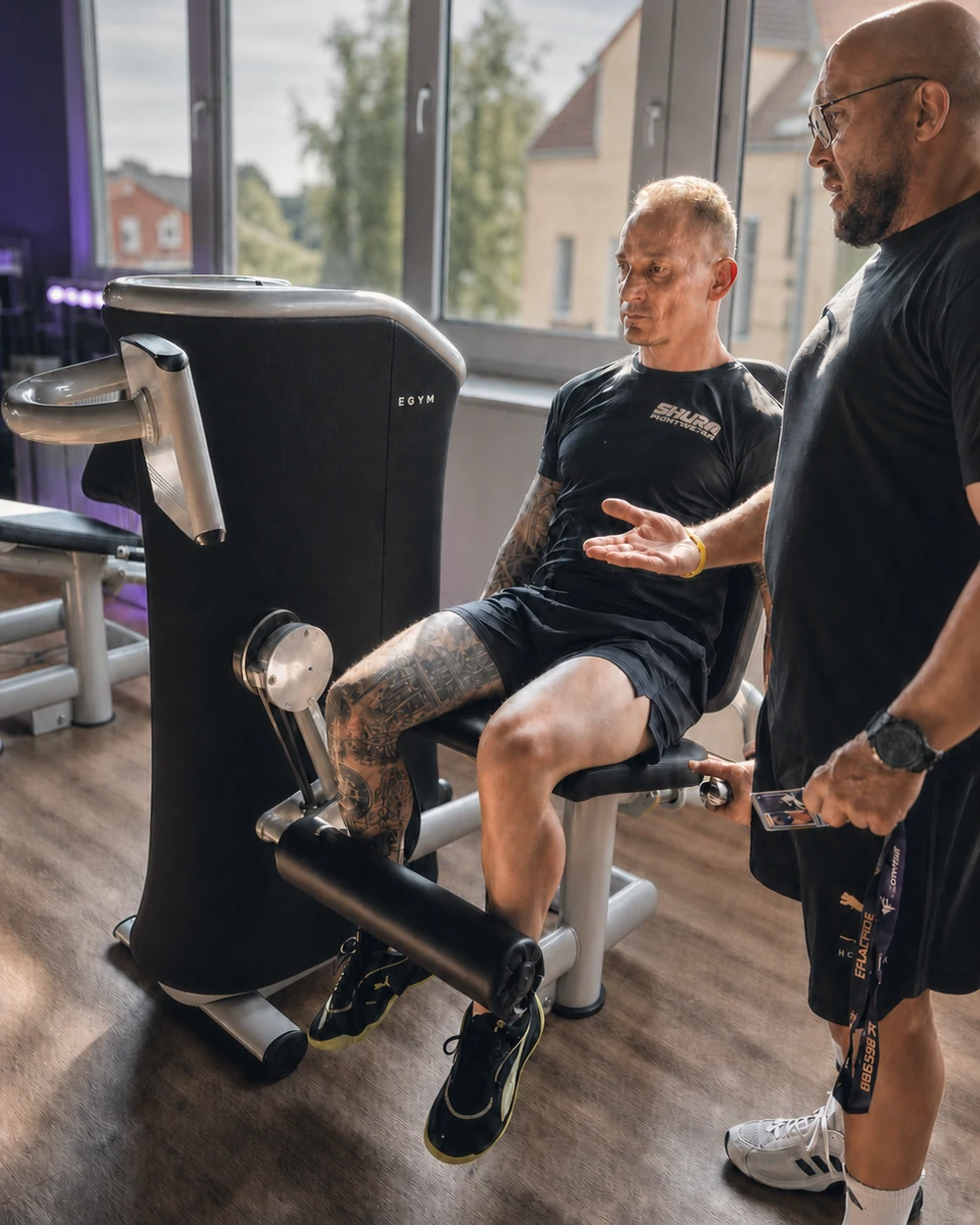 Trainer Mirko berät ein Mitglied am EGYM-Gerät im Fitnessstudio Hohenstein-Ernstthal – Lila Fitness