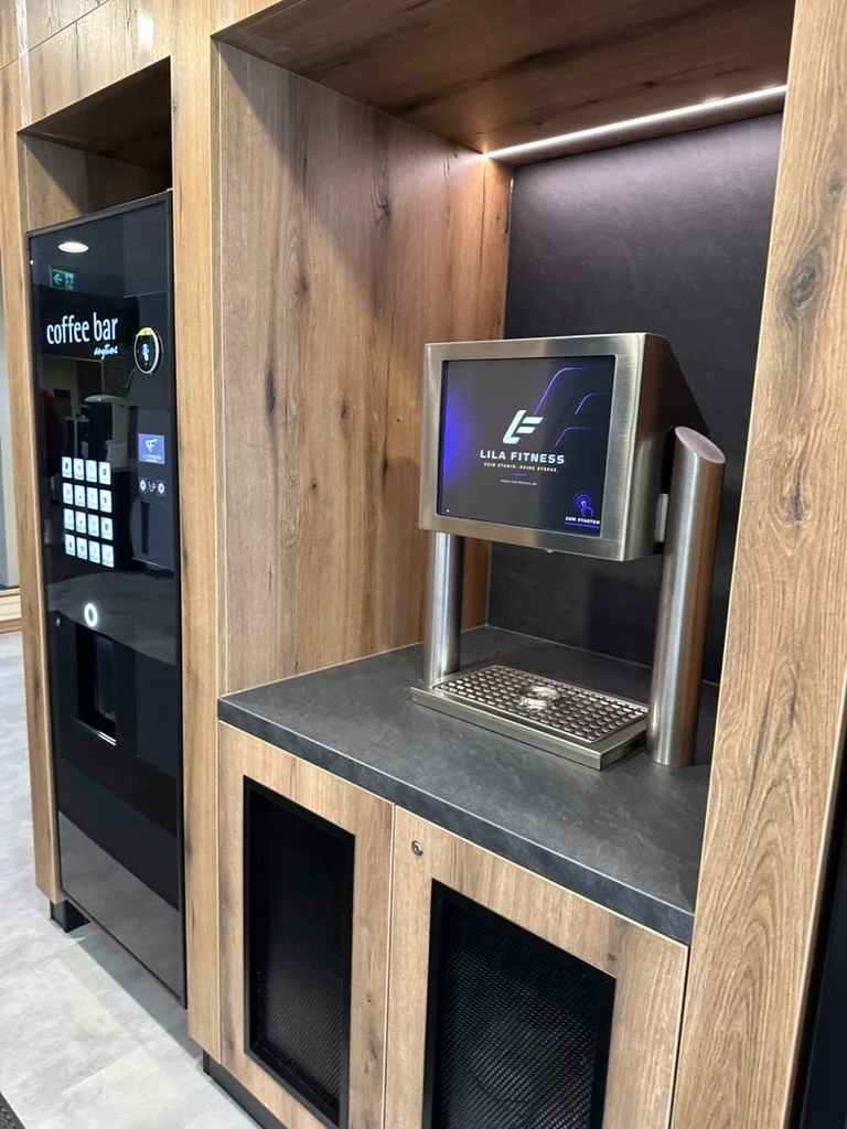 Check-in-Terminal mit Lila-Fitness-Display und Coffee Bar im Fitnessstudio Lichtenstein – Lila Fitness