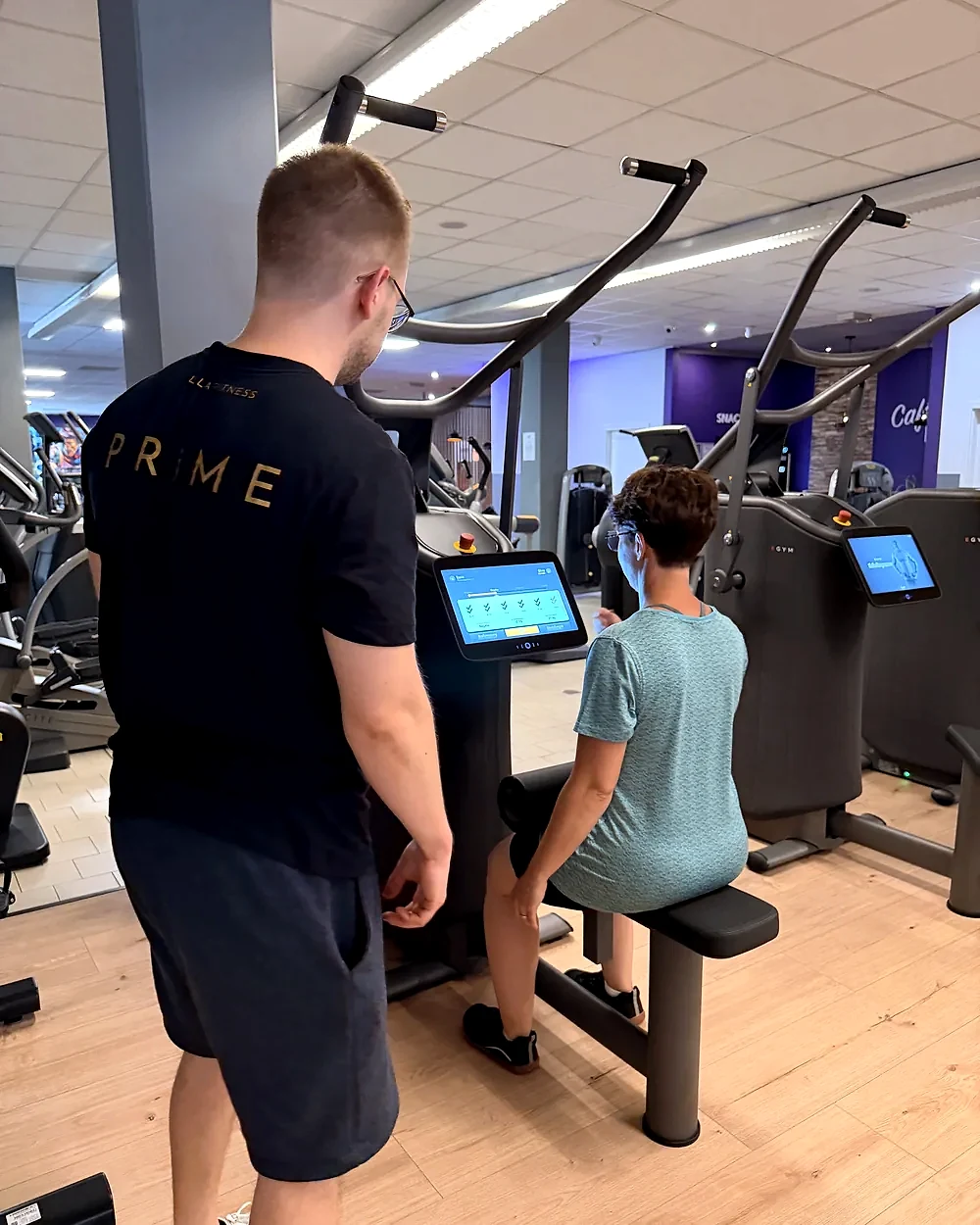 Trainer Yannic begleitet ein Mitglied beim Training am Latzug im Fitnessstudio Schwarzenberg – Lila Fitness