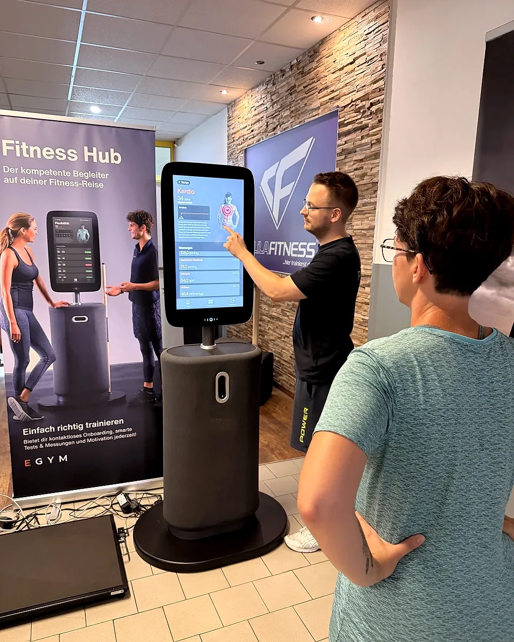 Trainer Yannic erklärt einem Mitglied den EGYM Bio-Check am Fitness Hub im Fitnessstudio Schwarzenberg – Lila Fitness