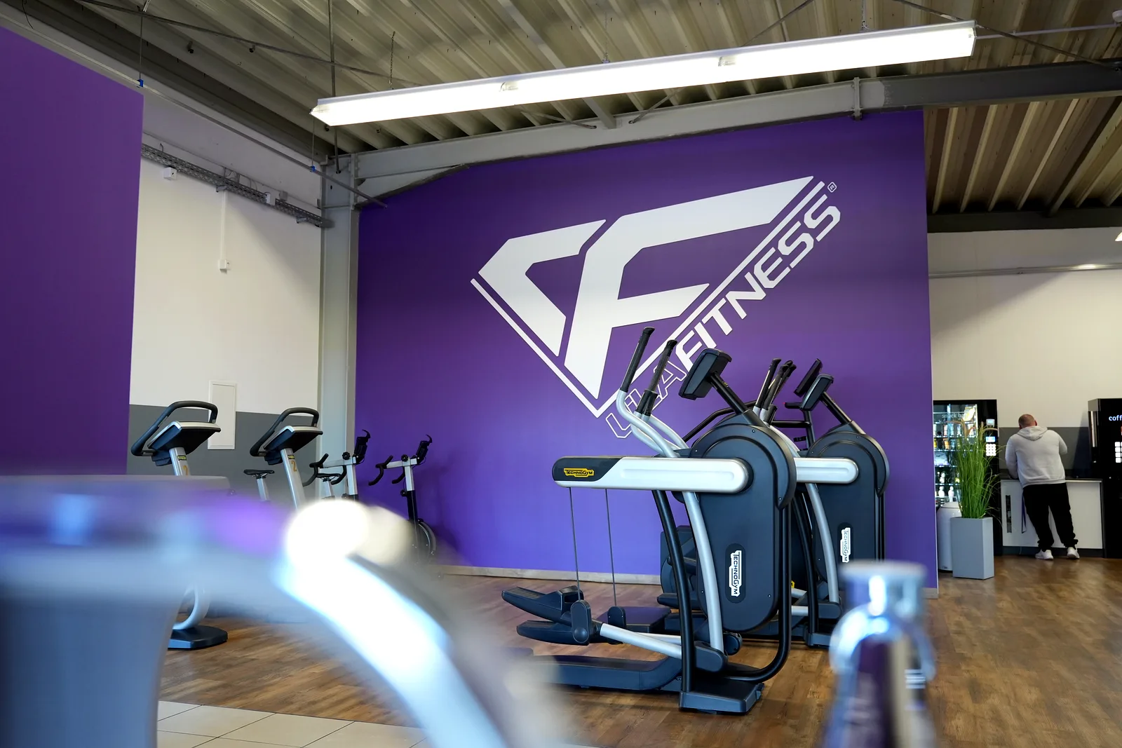 Trainingsfläche mit Cardiogeräten und Lila Fitness Markenwand im Fitnessstudio Stollberg