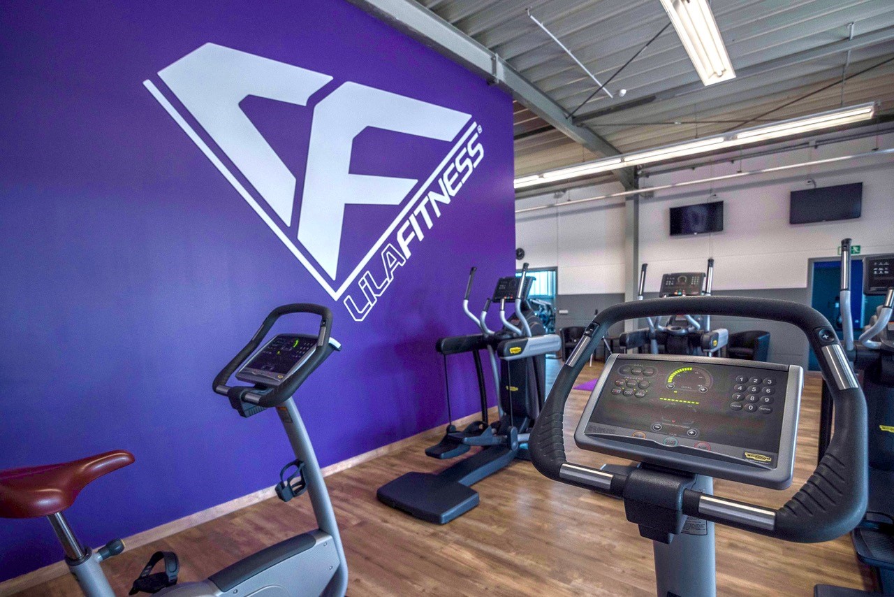 Einblick in den Cardio-Bereich im Fitnessstudio in Stollberg von Lila Fitness. Ergometer vor einer lila Wand mit Lila Fitness Logo.
